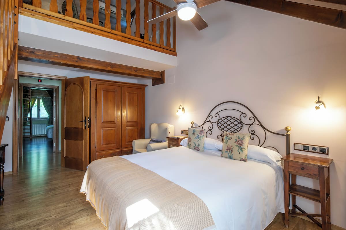 Quarto com cama grande, guarda-roupa de madeira e mezanino com escada de madeira.