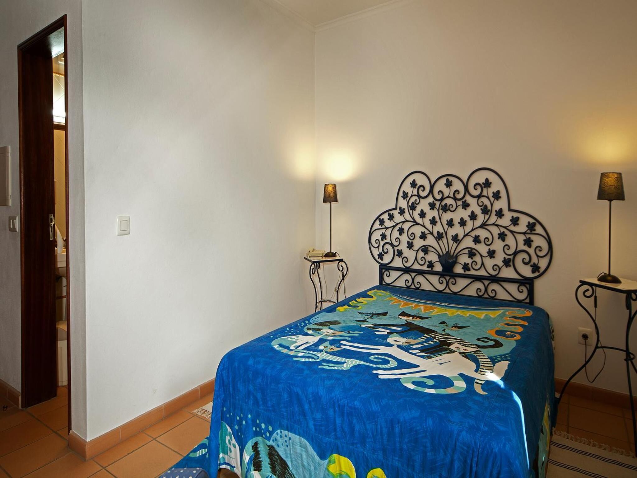 Ein Schlafzimmer mit einem Bett, zwei Nachttischlampen, einem dekorativen Kopfteil und einer Tür zu einem anderen Raum.