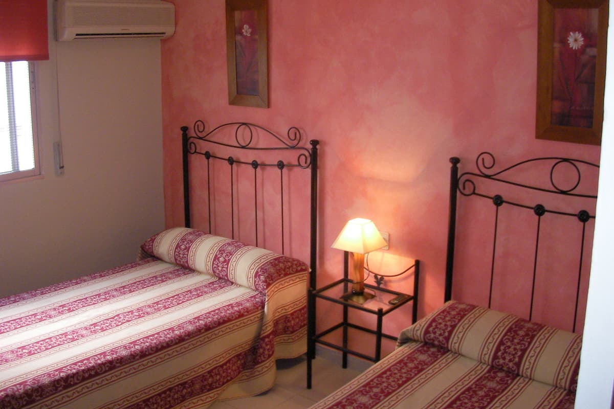 Un dormitorio con dos camas individuales, una mesita de noche con lámpara y aire acondicionado instalado en la pared.