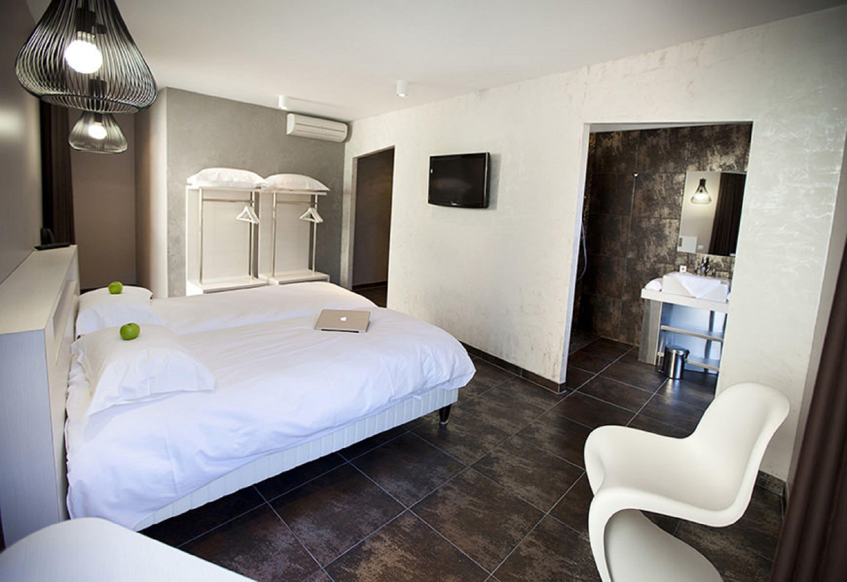 A modern hotel room with a large bed, a desk, a chair, a TV, and a bathroom visible through an open door.