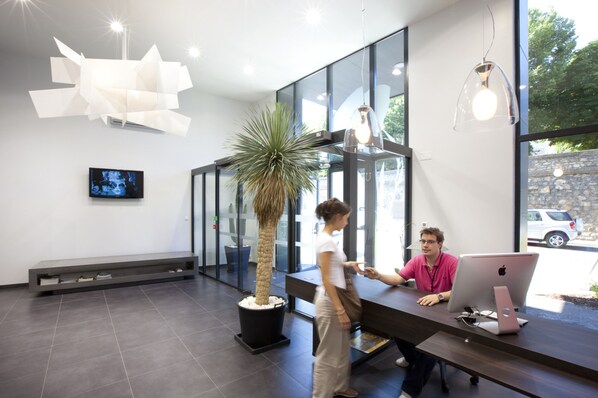 A modern interior with a reception desk, a large potted plant, and a television screen.