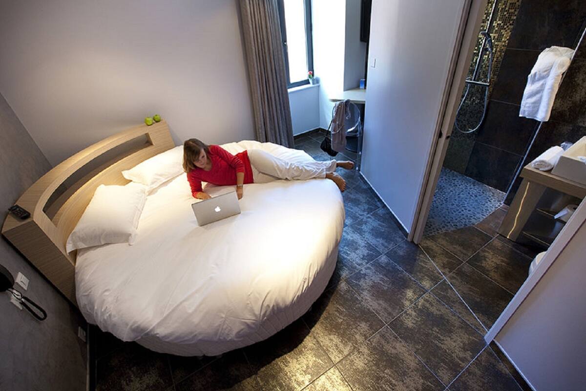 A modern hotel room with a curved bed, a laptop, and a shower area.