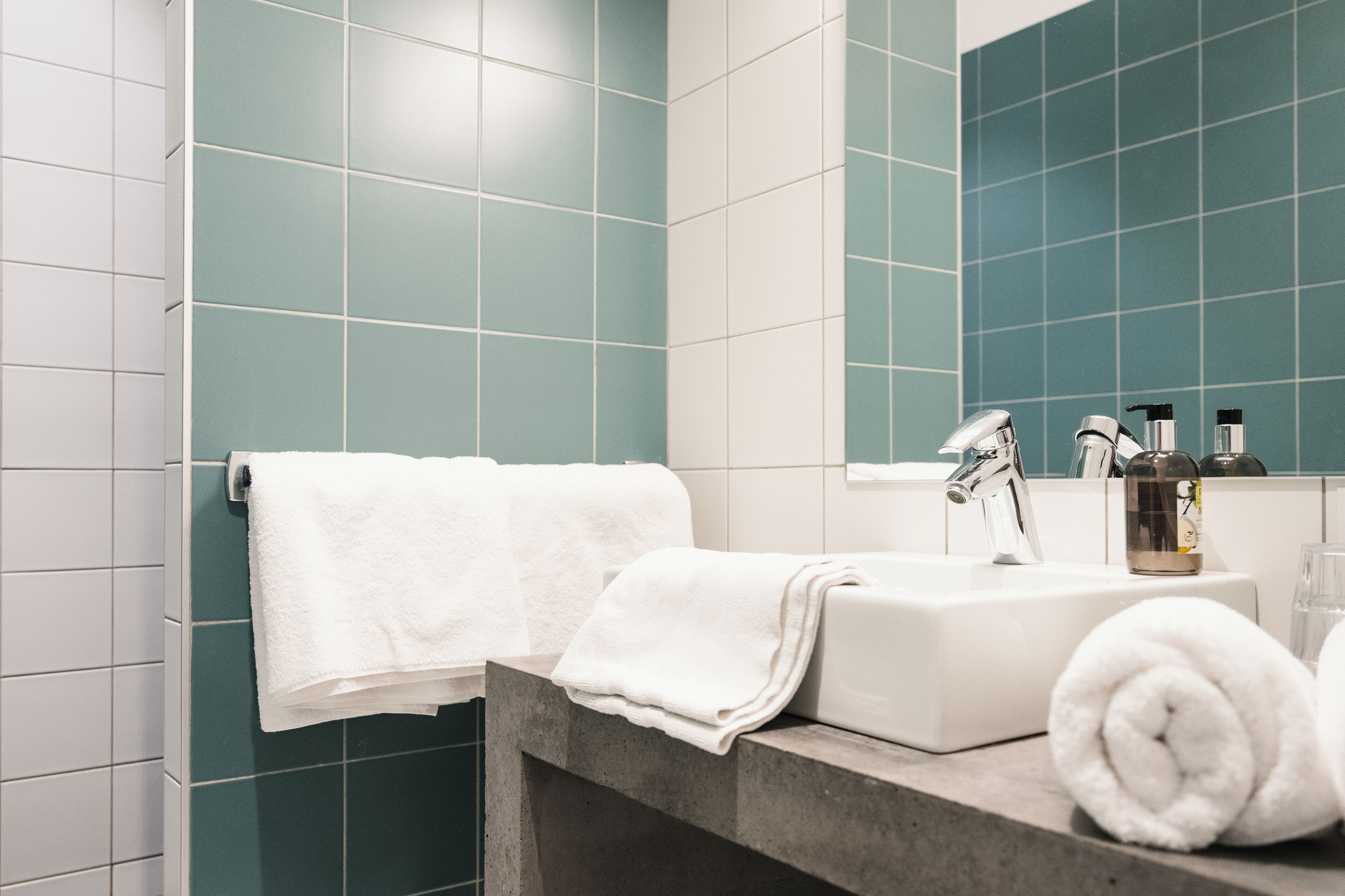 A bathroom with teal tiles, a white sink, a mirror, and a towel rack.