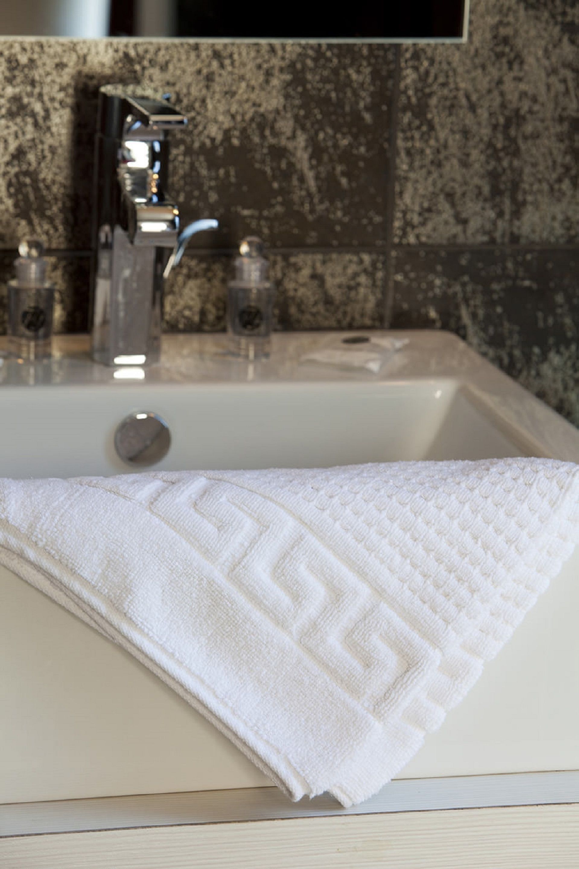A bathroom sink with a white towel and a glass of water.