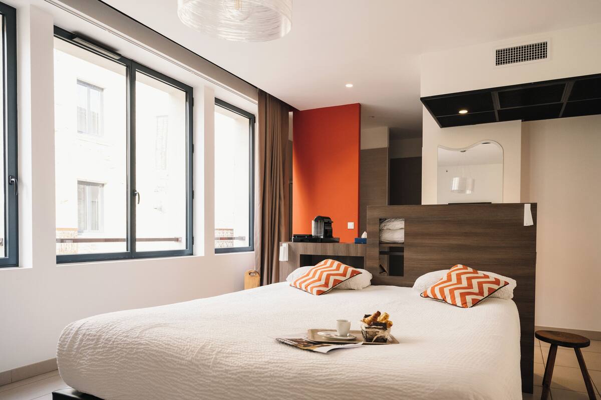 A hotel room with a large bed, a coffee machine, and a view of the city through the window.