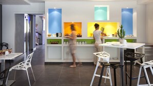 Un restaurante moderno con un interior luminoso, una decoración en tonos blanco y verde, y una barra donde dos personas sirven comida.