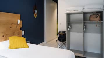 A hotel room with a wooden headboard, a yellow pillow, a wardrobe with a handbag, and a wall-mounted light fixture.