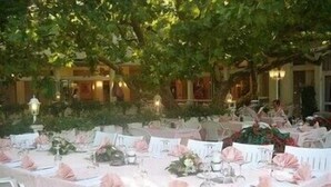 Un espace de restauration en plein air avec des tables dressées pour un repas, entouré de verdure et avec un bâtiment en arrière-plan.