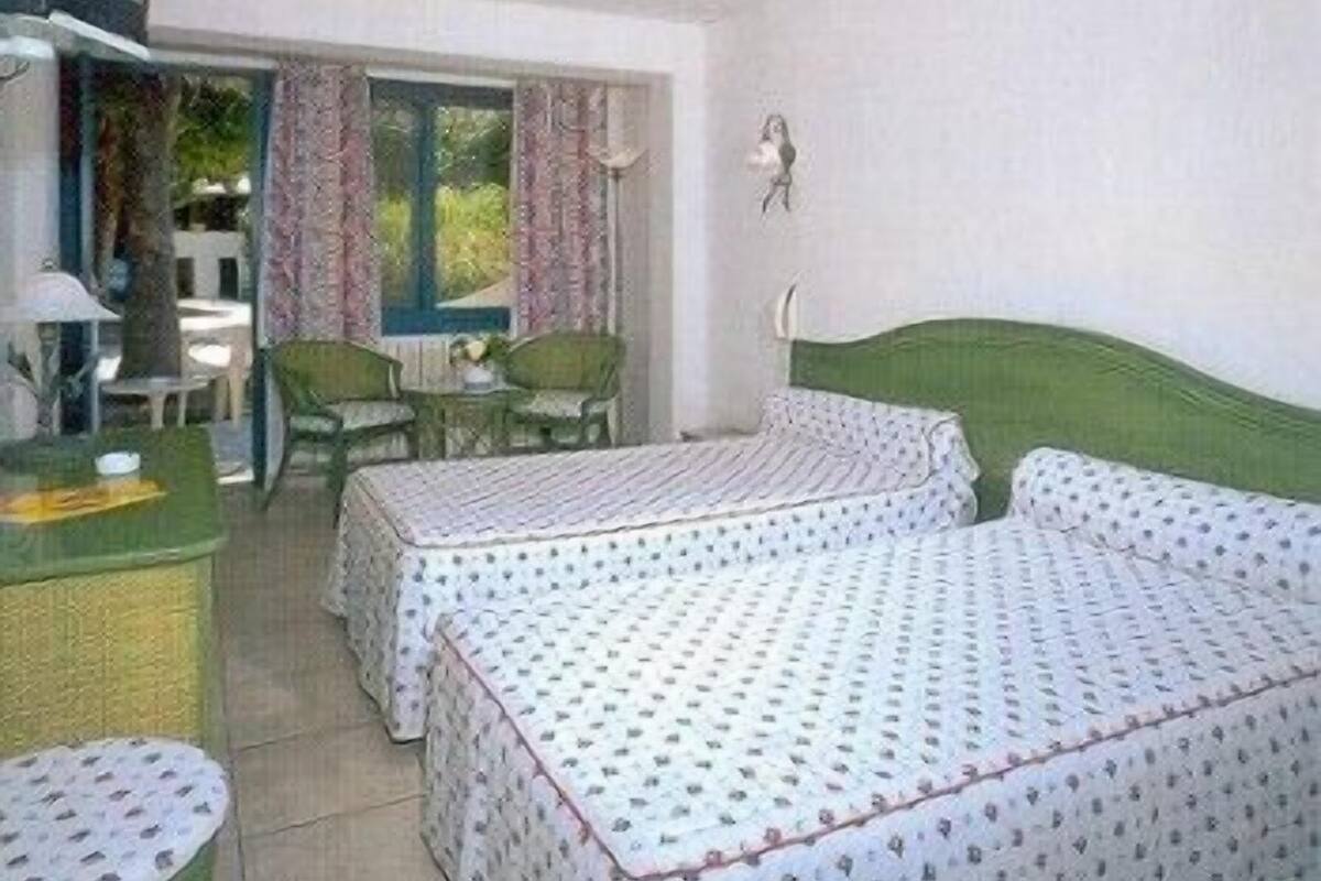 A room with two single beds, a small table, a chair, and a television.