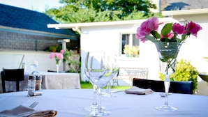 A table set for dining outdoors with a clear glass vase containing pink flowers, a water pitcher, and wine glasses. - Chez Germaine (Geus-d'Oloron)