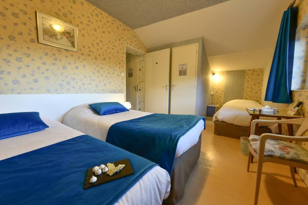 A hotel room with two beds, a chair, a small table, and a wardrobe.