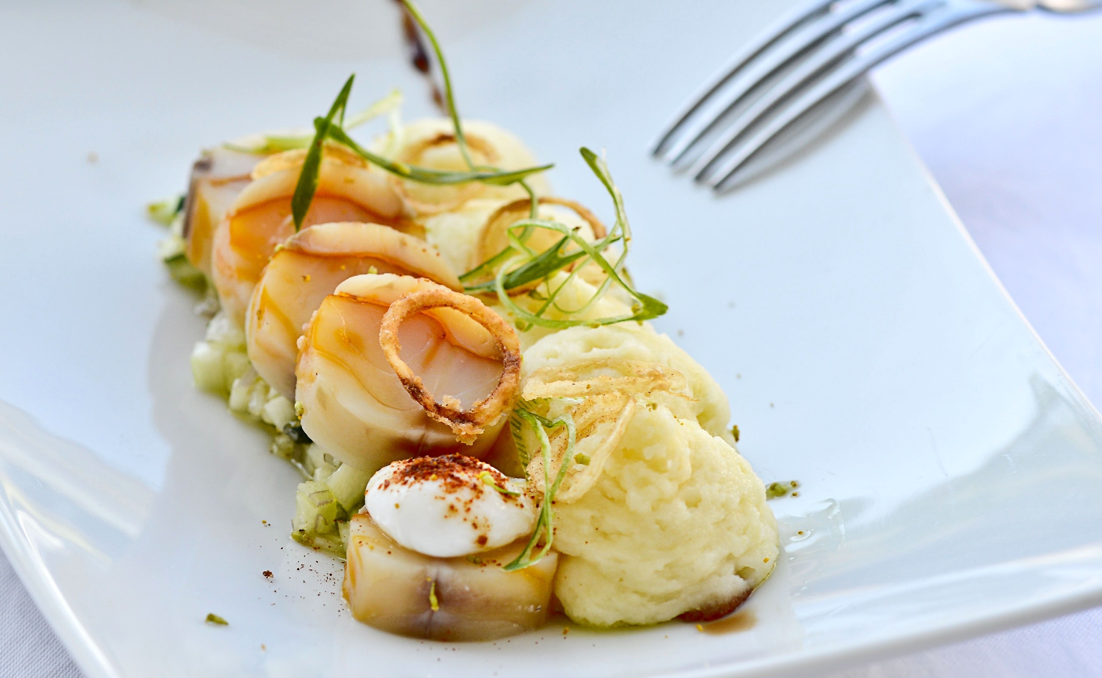 A plate of food with scallops, mashed potatoes, and garnishes.