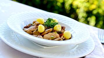 Ein weißer Teller mit einem Gericht aus Fleisch und Kartoffeln, garniert mit Petersilie, auf einem Tisch mit weißer Tischdecke.