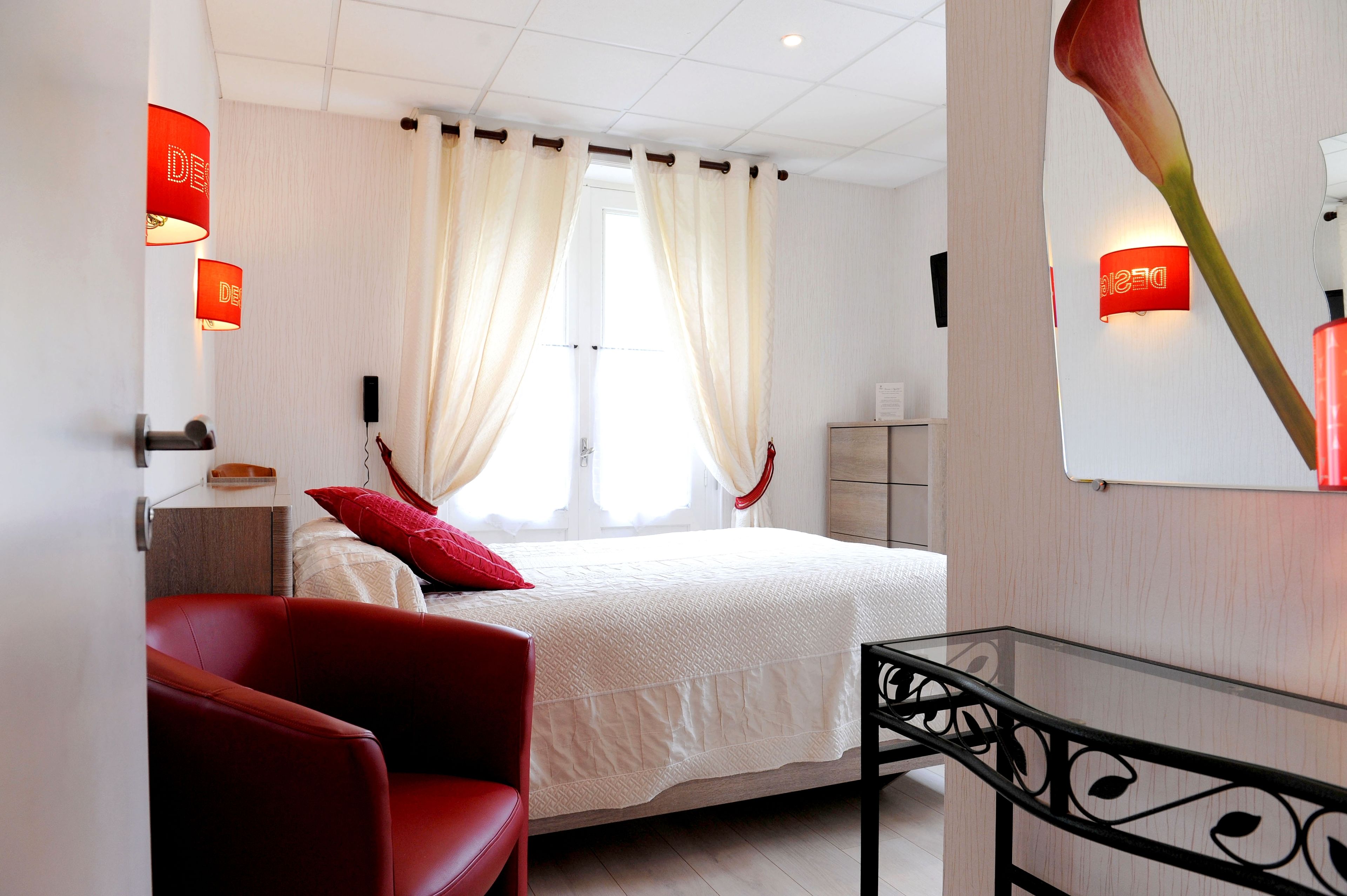 Une chambre d’hôtel avec un lit, une chaise rouge, une table en verre et des lampes rouges.
