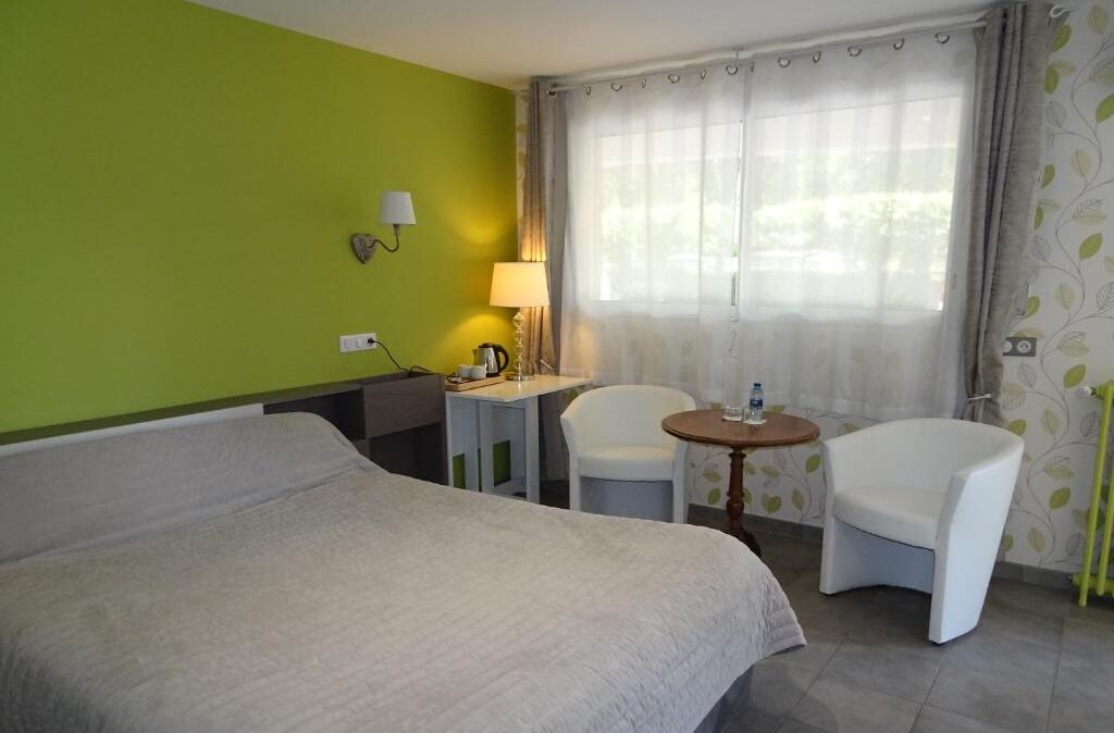 A hotel room with a bed, two chairs, a small table, a lamp, and a window with curtains.