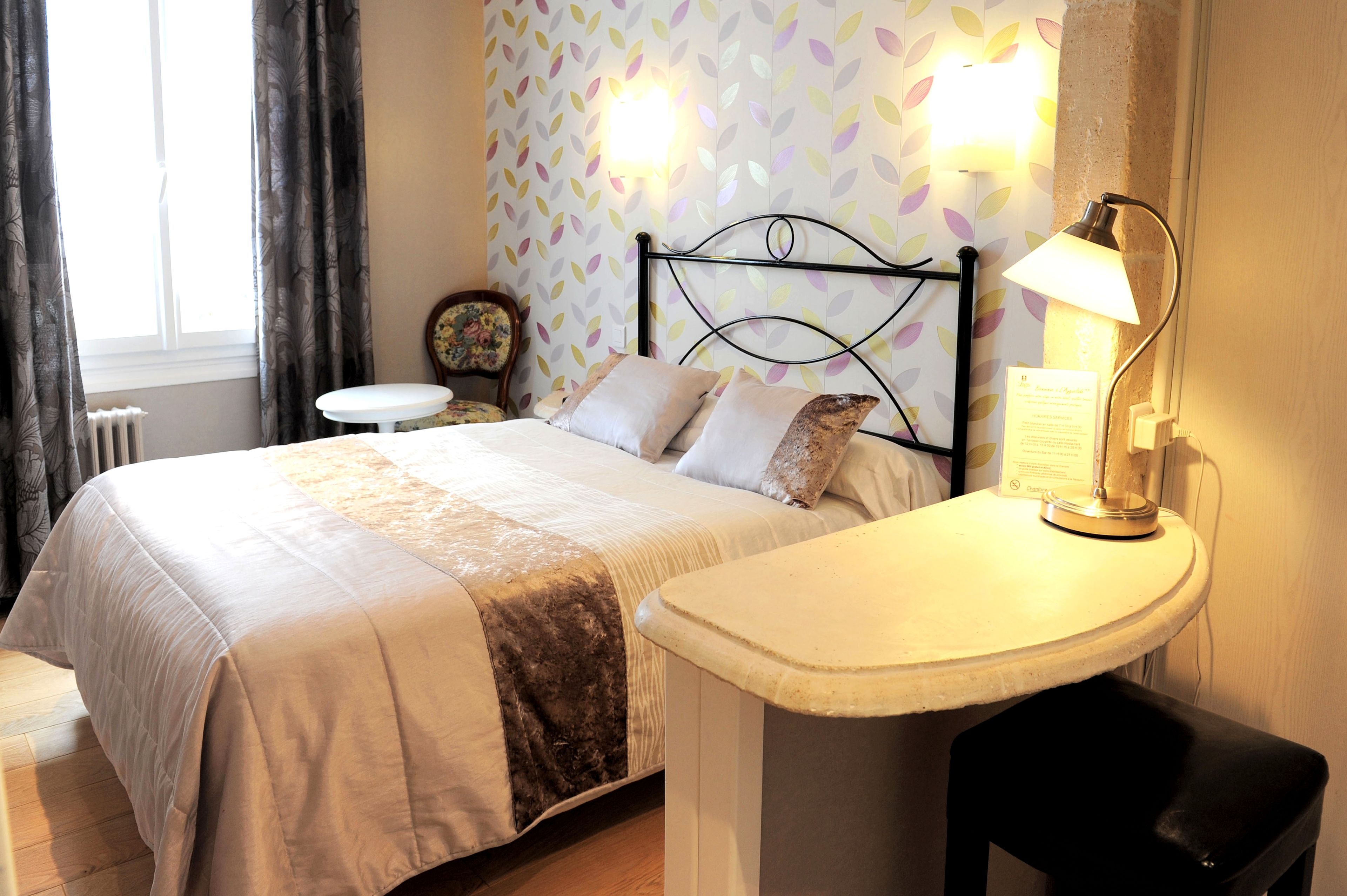 A neatly made bed with a headboard, a bedside table with a lamp, and a small round table with a chair.