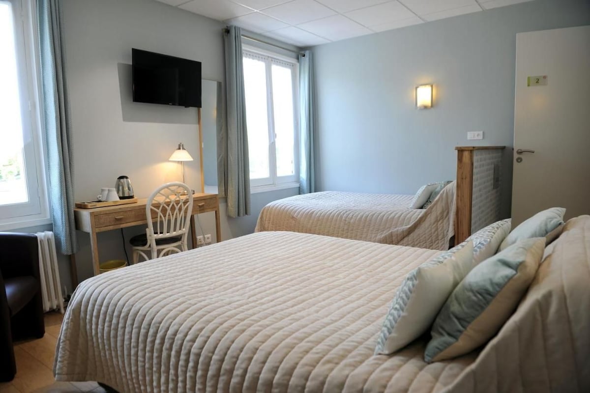 A hotel room with two beds, a desk, a chair, a television, and a window with curtains.