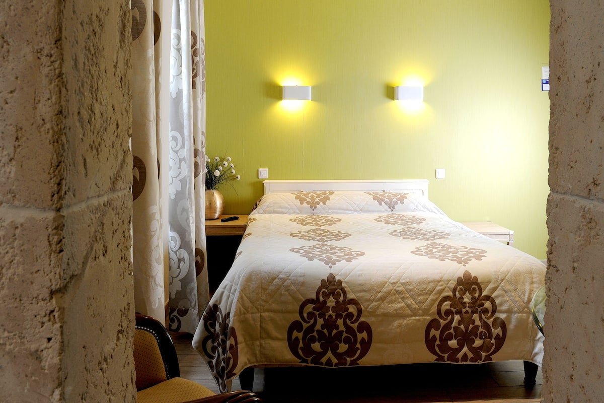 A hotel room with a bed, a nightstand, a vase with flowers, and two wall-mounted lights.