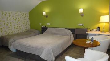 A hotel room with two beds, a small round table with a chair, a desk with a lamp, and two wall-mounted lamps.