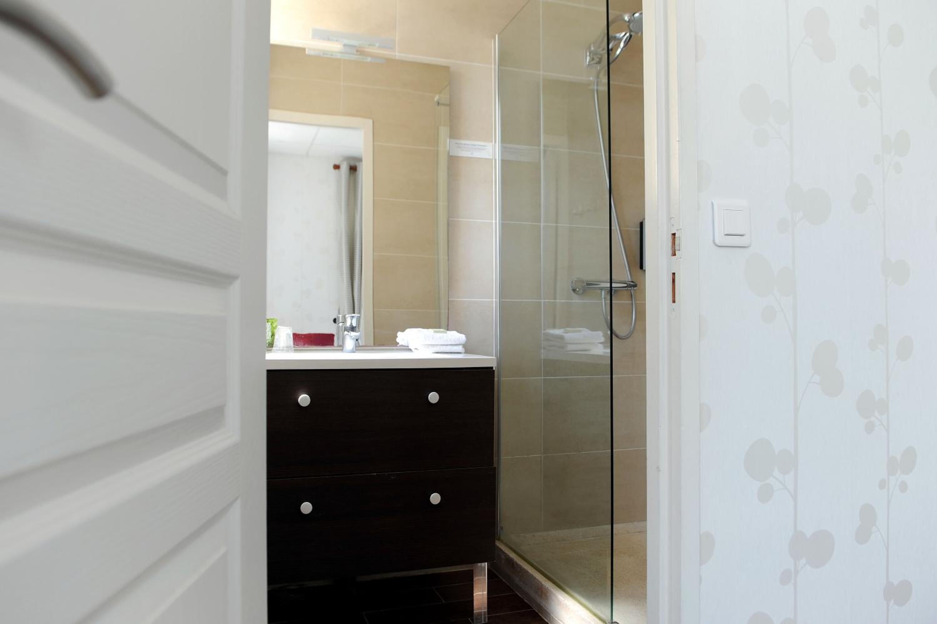 A bathroom with a glass shower enclosure, a white vanity with a mirror, and a beige tiled wall.