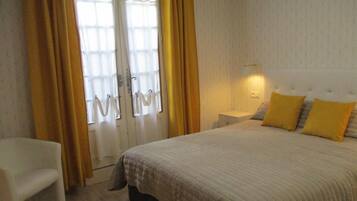 A bedroom with a bed, a nightstand, a chair, and a window with curtains.