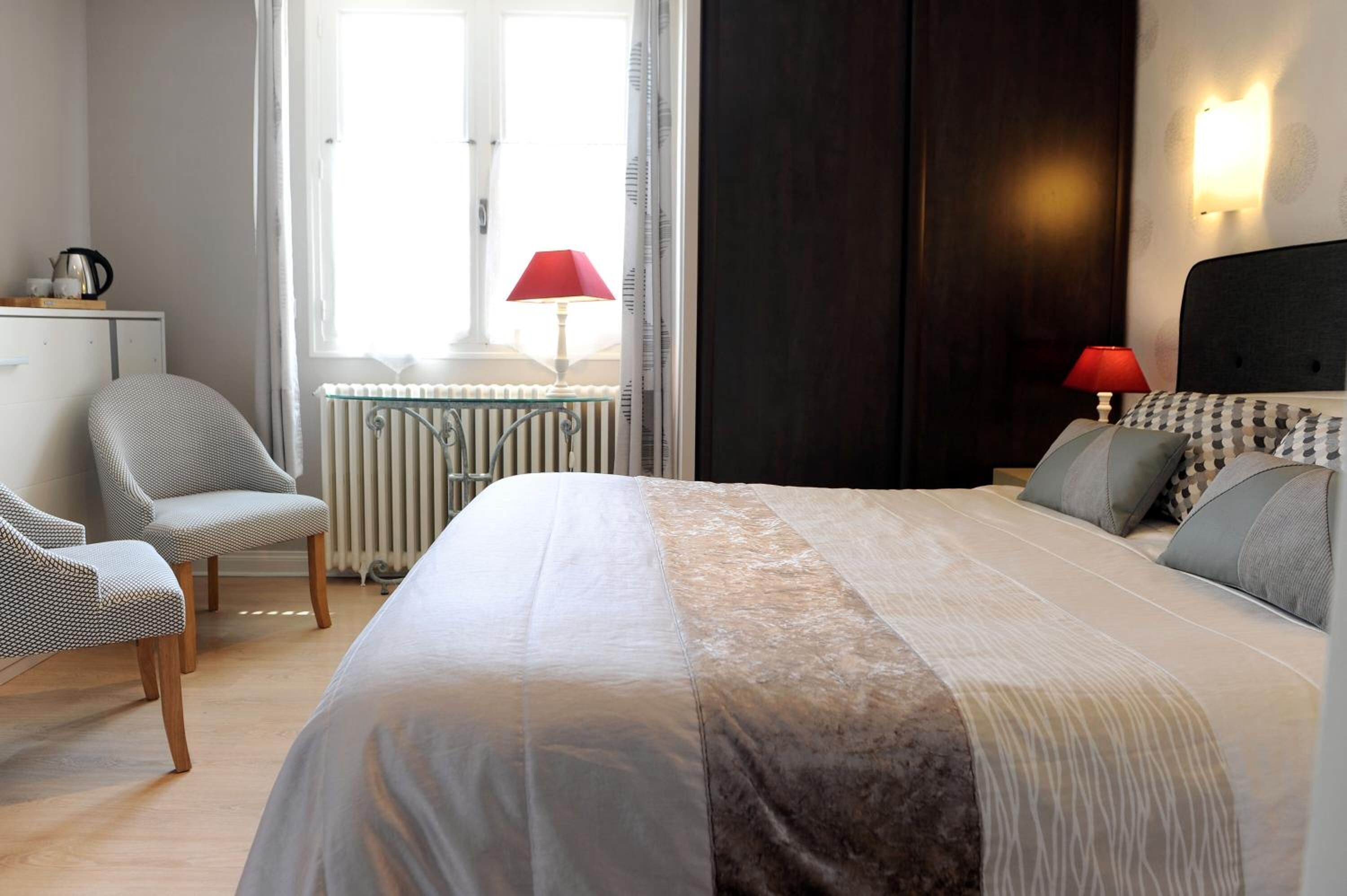 Une chambre à coucher avec un lit, deux chaises, un radiateur et une fenêtre avec des rideaux.