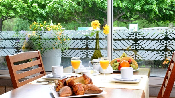A breakfast table with croissants, fruit, juice, and a vase of flowers. - L'Ayguelade (Bielle)