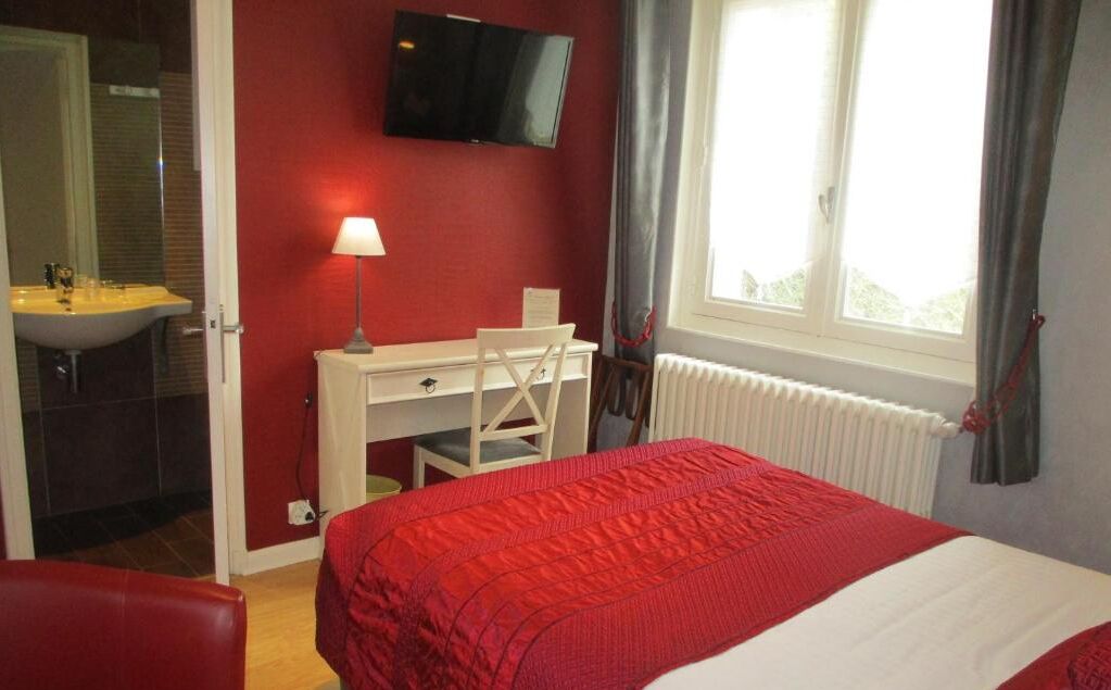 Une chambre à coucher avec un lit, un bureau, une chaise, une télévision et une fenêtre avec des rideaux.