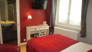 Une chambre à coucher avec un lit, un bureau, une chaise, une télévision et une fenêtre avec des rideaux.