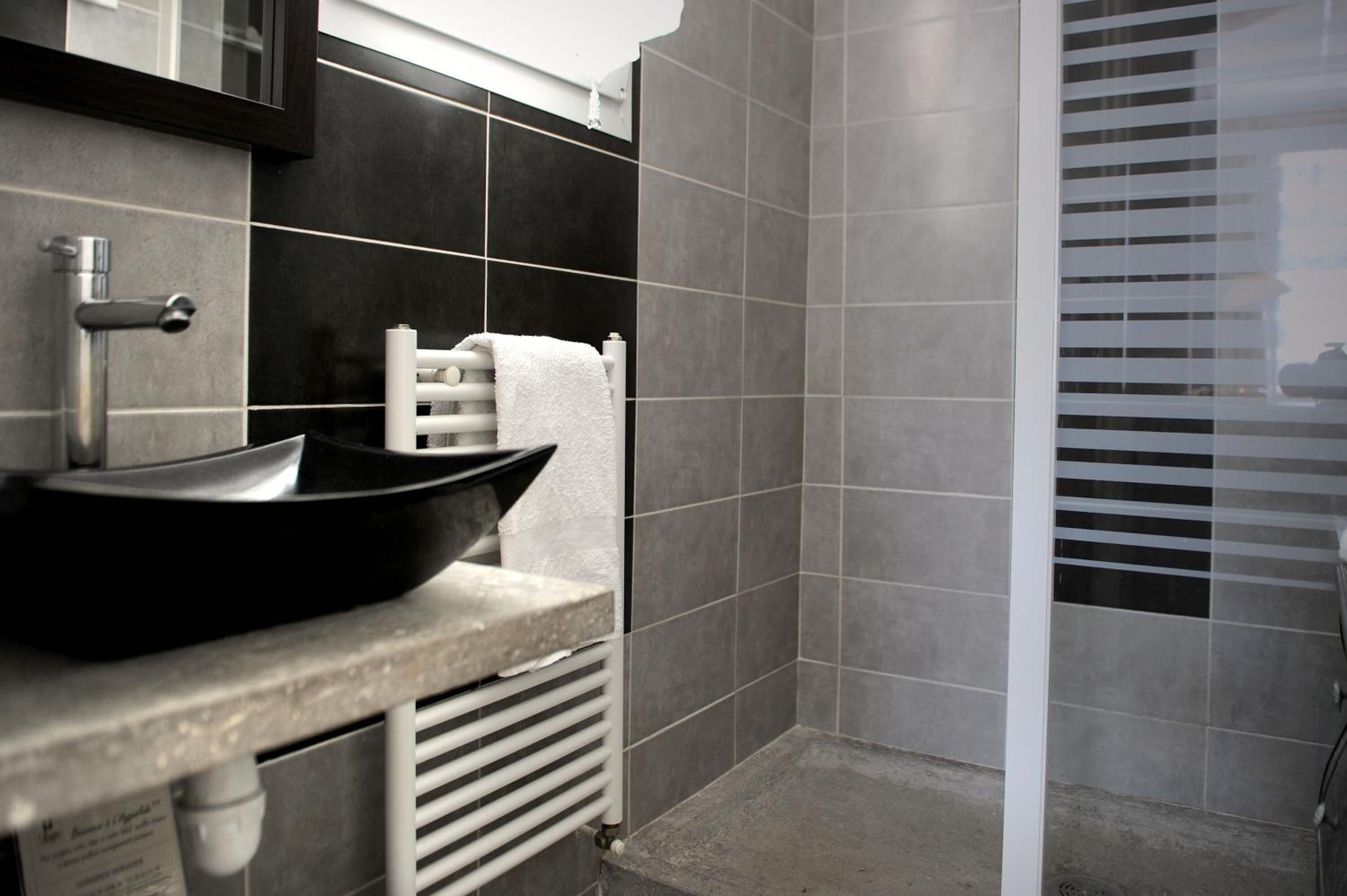 Un baño con un lavabo tipo recipiente negro, un perchero y una ventana con persianas.