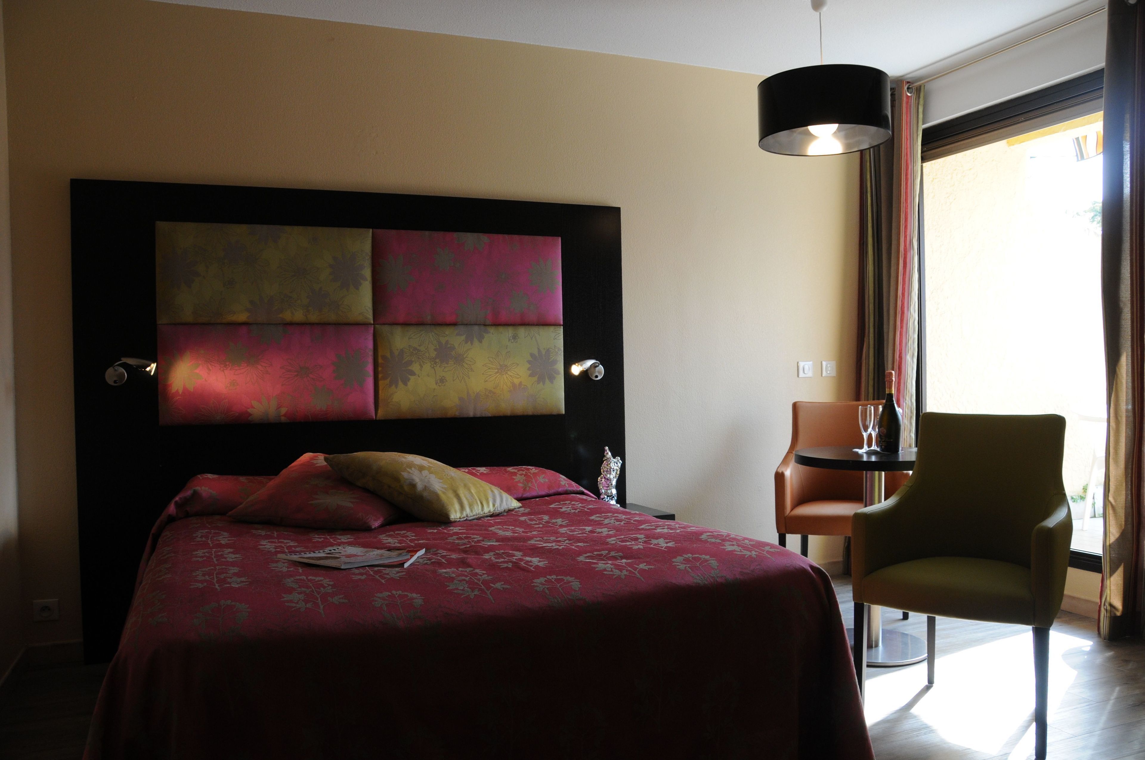 Una habitación de hotel con una cama grande, una silla, una mesa y un ventanal con cortinas.