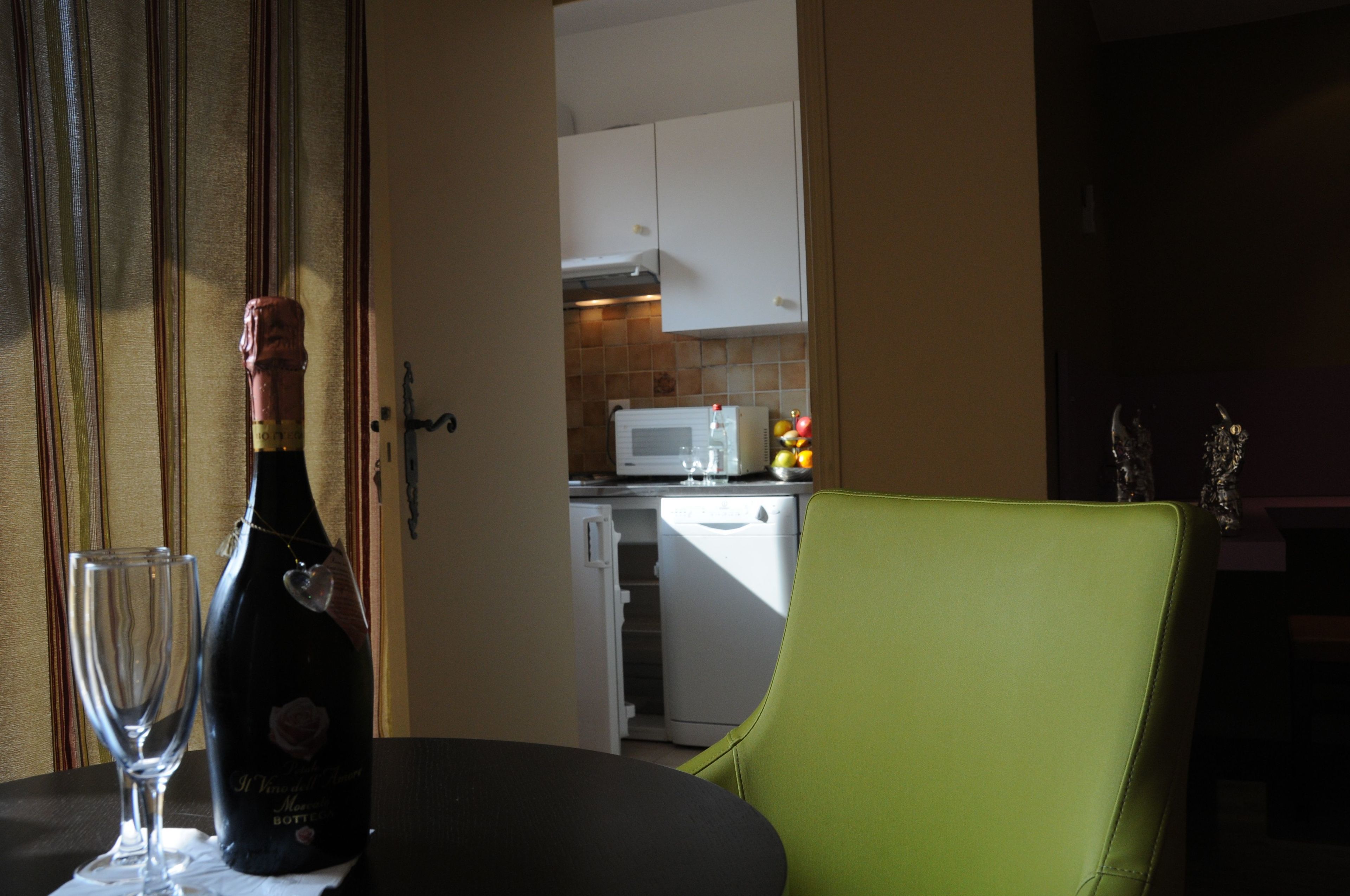 A dining area with a table, a bottle of champagne, and a glass. A green chair is visible.