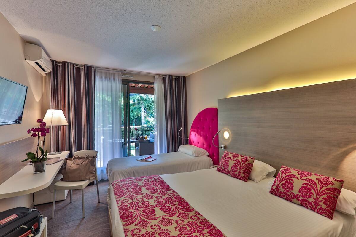 A hotel room with two beds, a desk, a chair, a TV, and a window with curtains.