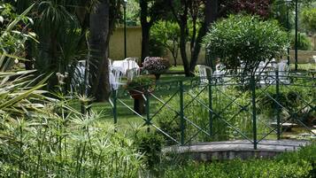 Un jardin avec une clôture en métal, des chaises blanches et un pot de fleurs.