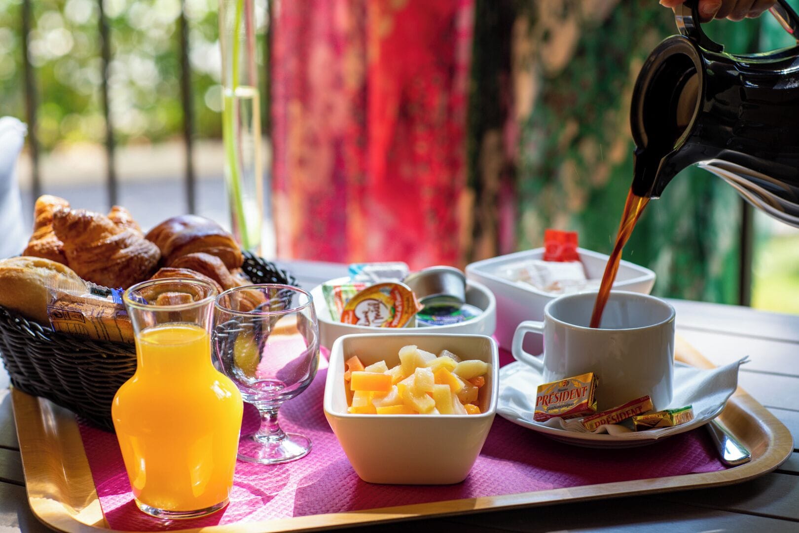 Una bandeja de desayuno con croissants, zumo de naranja, un bol de fruta, una taza de café y un pastel.