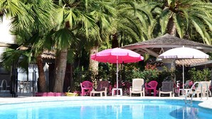 A pool area with lounge chairs and umbrellas, surrounded by palm trees and a building in the background.