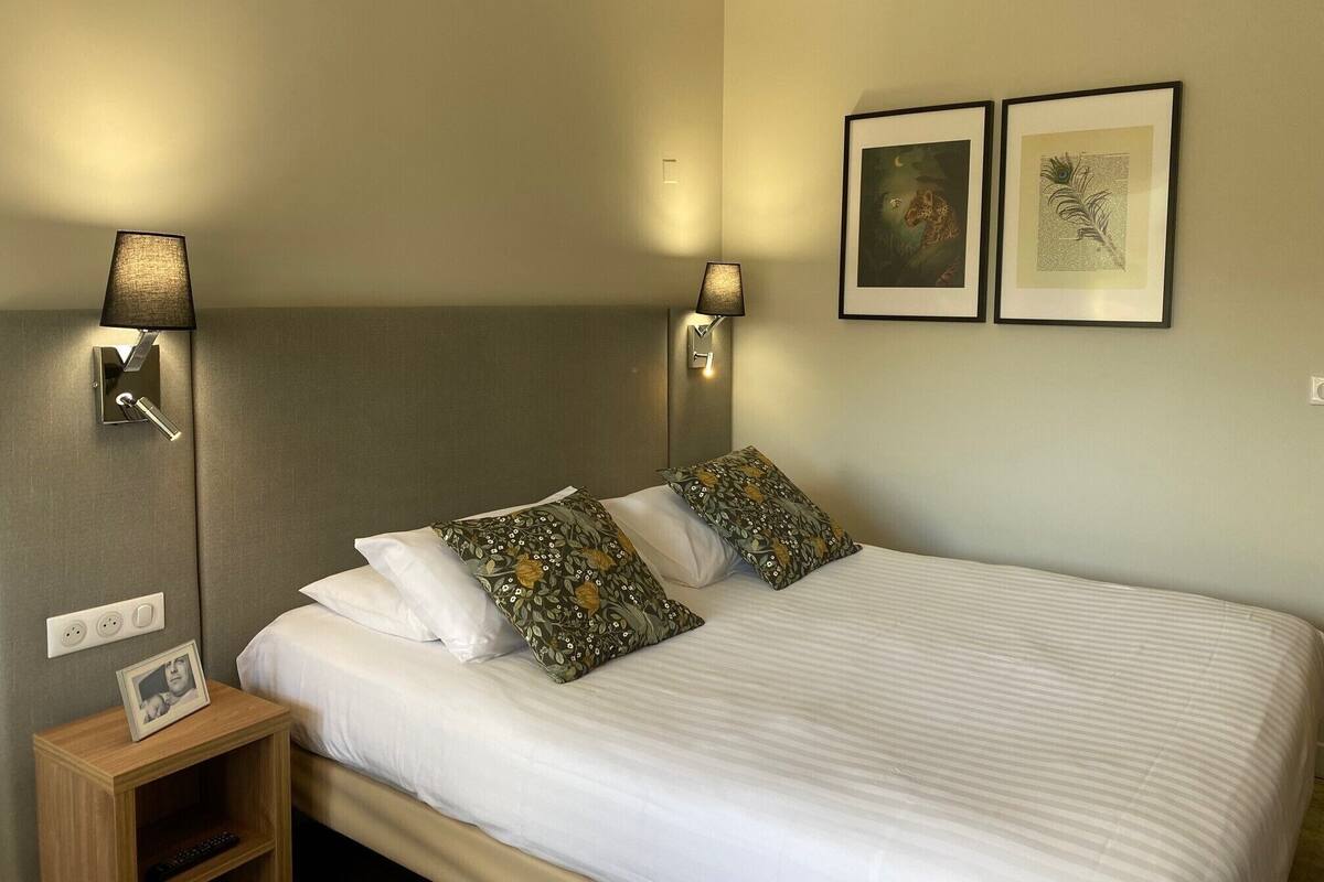 A neatly made bed with white linens and patterned pillows, a bedside table with a lamp, and two framed pictures on the wall.