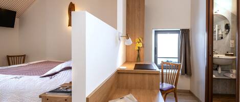 A modern bedroom with a bed, a desk, and a chair. There is a wooden bench, a small table, and a mirror.