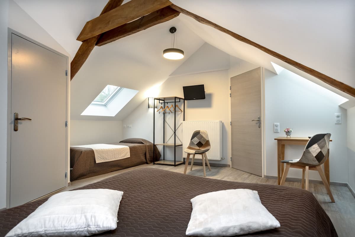 Un dormitorio con techo inclinado, una cama con dos almohadas, una silla, un escritorio y un televisor montado en la pared.