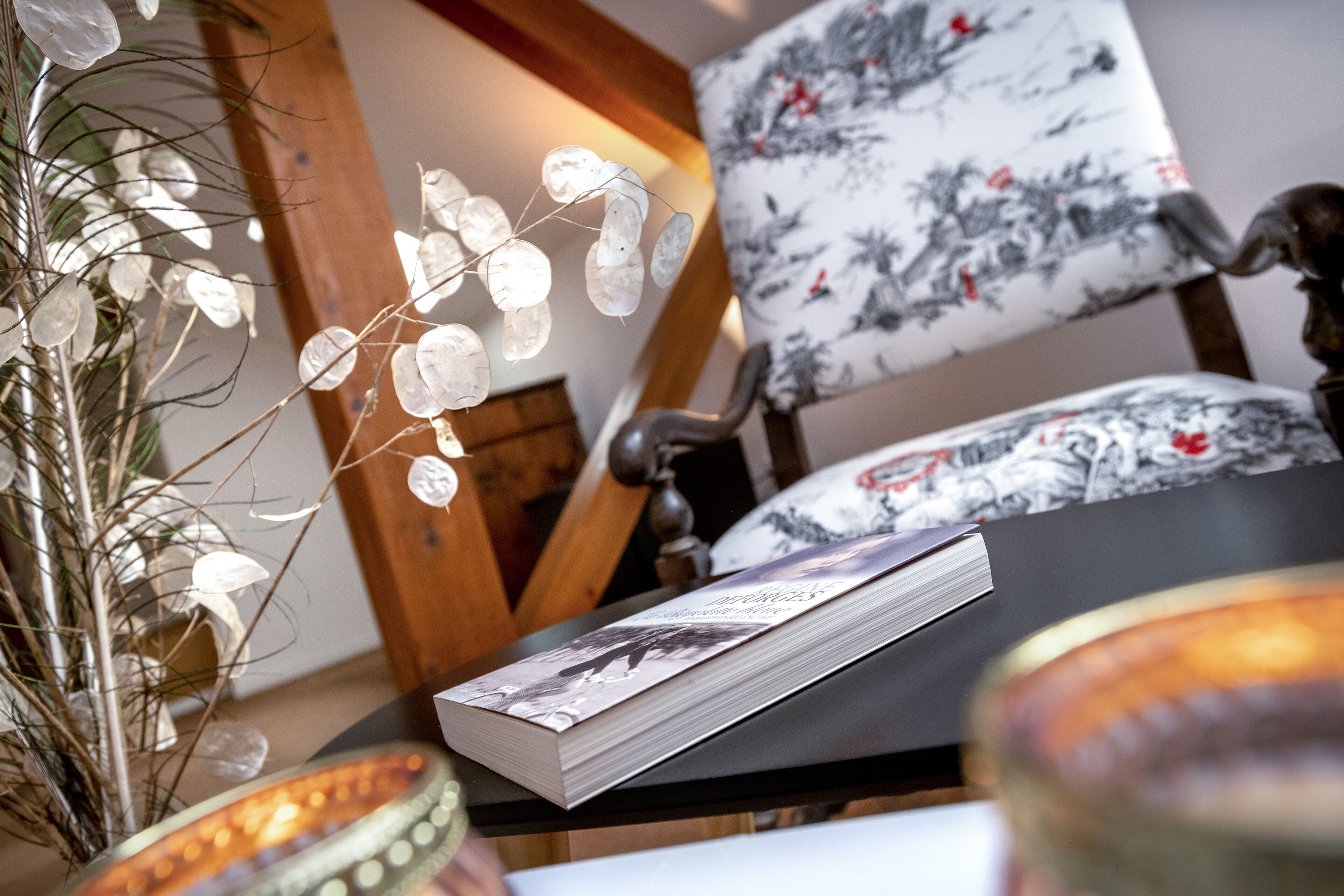 A book on a table, a chair with floral upholstery, and a decorative plant with glass elements.