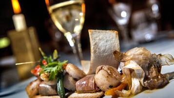 A gourmet dish with various meats and vegetables, accompanied by a glass of white wine and a lit candle.