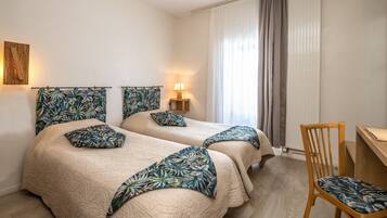Habitación de hotel con dos camas, una silla de madera, un escritorio y una ventana con cortinas.