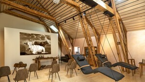 A spacious room with wooden beams, a large painting of a cow, and multiple reclining chairs. - Hôtel Restaurant de la Poste et La Grange Détente, espace bien-être (Chateauneuf-de-Randon)