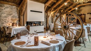 A rustic dining area with round tables, wooden beams, stone walls, and a large wooden wheel. - Hôtel Restaurant de la Poste et La Grange Détente, espace bien-être (Chateauneuf-de-Randon)