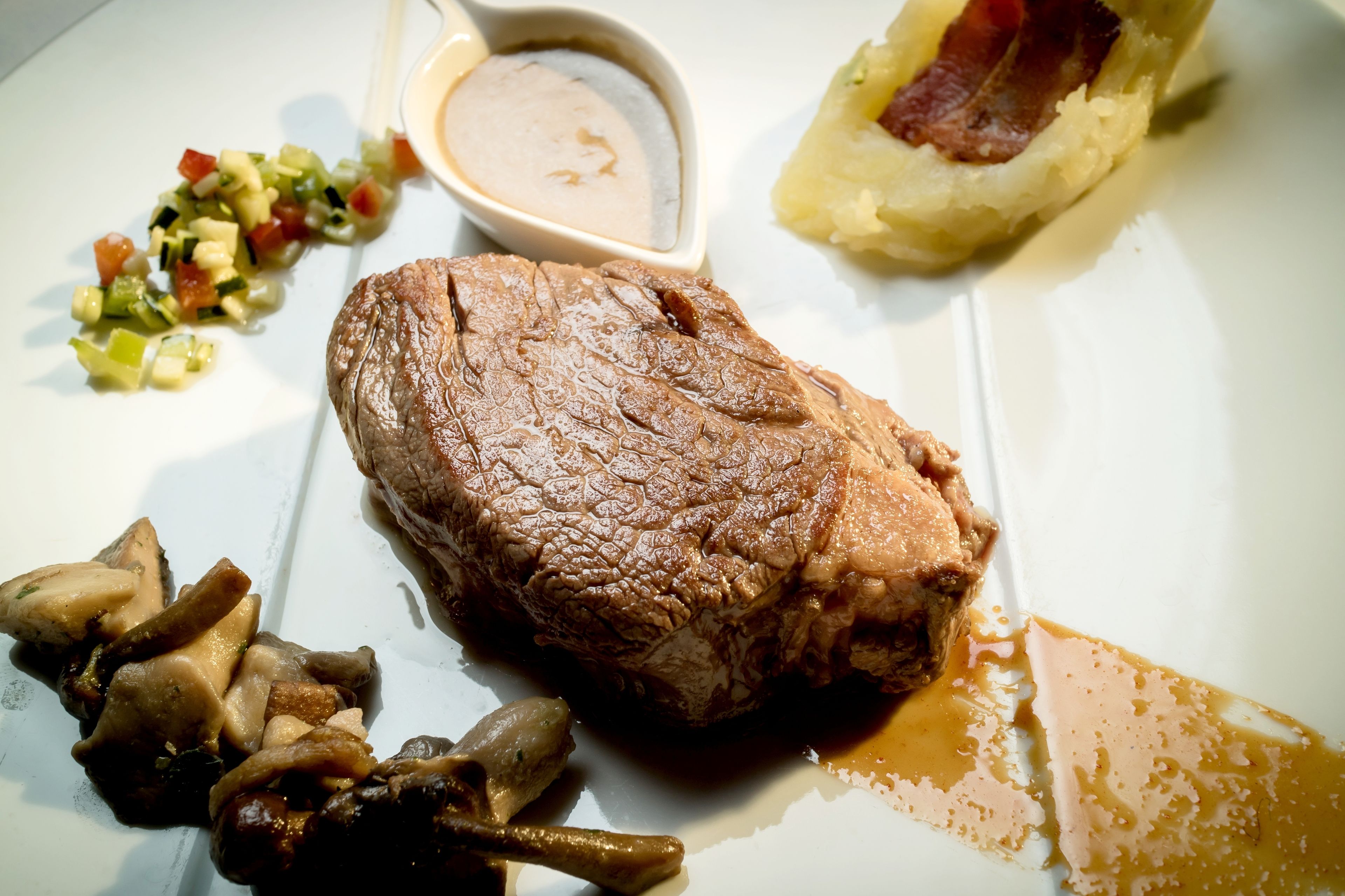 Um prato com um pedaço grande de carne, uma pequena tigela de molho e alguns vegetais.