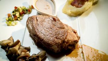 Um prato com um pedaço grande de carne, uma pequena tigela de molho e alguns vegetais.