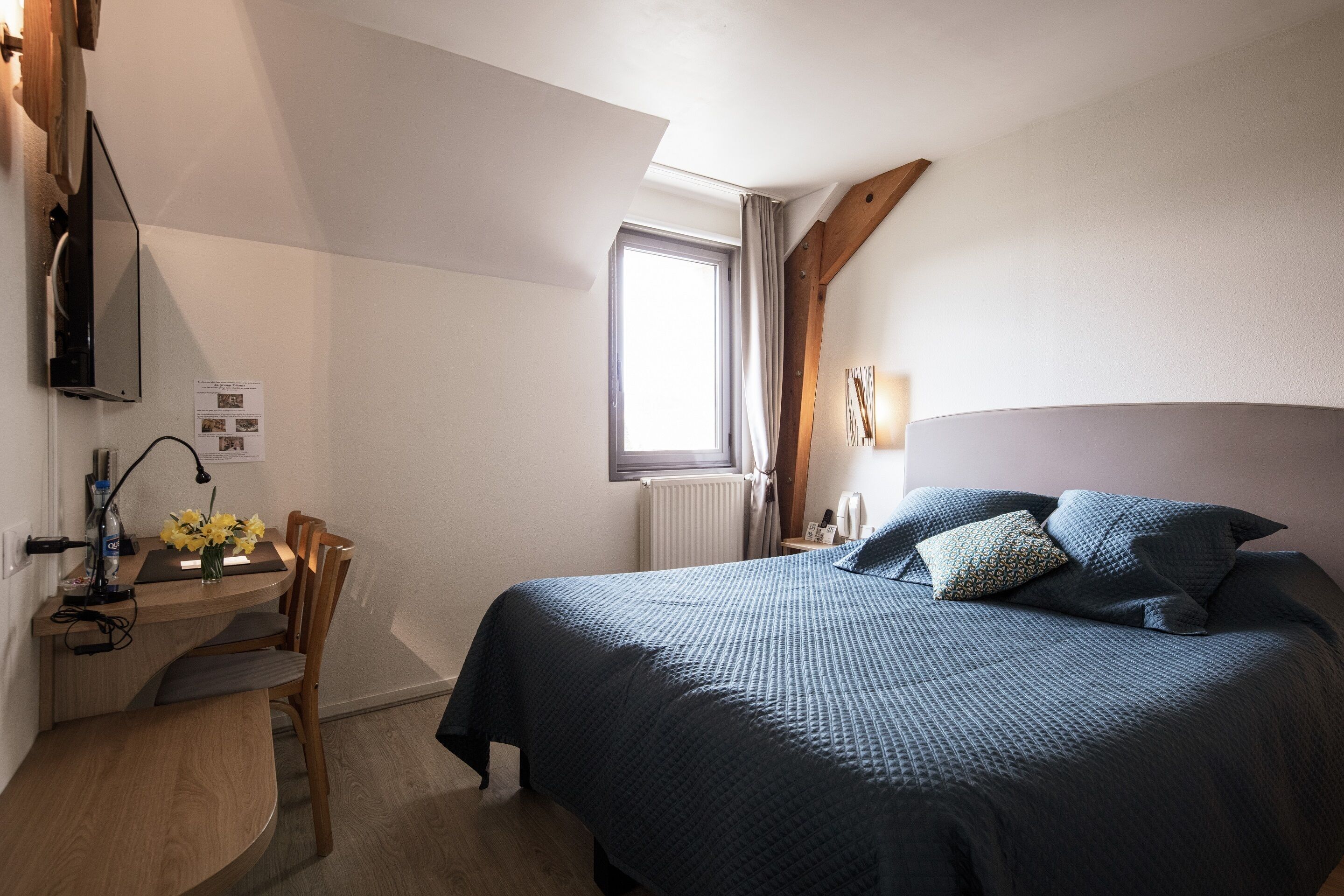 A bedroom with a bed, a desk, a chair, and a window.