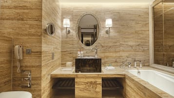 Un baño moderno con pared de mármol, un espejo ovalado grande, tocador doble, bañera y retrete.