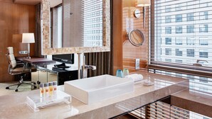 A modern bathroom with a large mirror, a sink, a chair, and a desk with a computer.