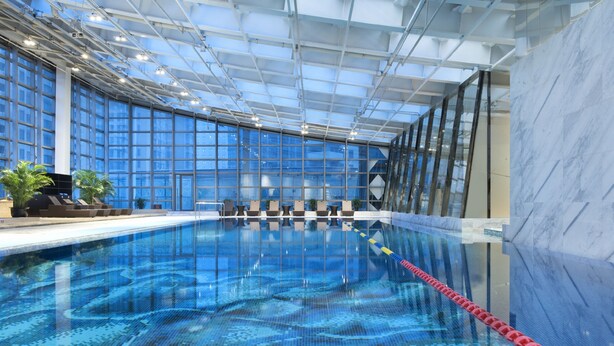 An indoor swimming pool with clear blue water, surrounded by large windows and a modern ceiling structure.
